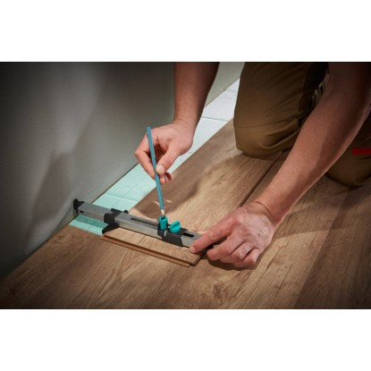 Wolfcraft sada pre montáž laminátu: Remeselník označuje laminát montážnym nástrojom proti stene. Wolfcraft sada pre montáž laminátu: Remeselník označuje laminát montážnym nástrojom proti stene.