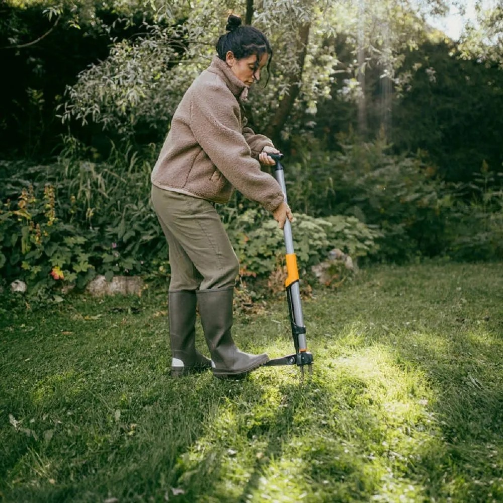 Žena používa vytrhávač buriny Fiskars Ergonomic v záhrade na odstraňovanie buriny. Žena používa vytrhávač buriny Fiskars Ergonomic v záhrade na odstraňovanie buriny.