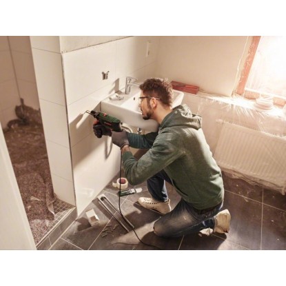 Muž vŕta do steny v kúpeľni s príklepovou vŕtačkou Bosch EasyImpact 5500. Muž vŕta do steny v kúpeľni s príklepovou vŕtačkou Bosch EasyImpact 5500.
