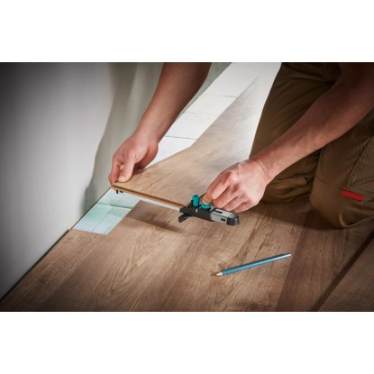Wolfcraft sada pre montáž laminátu: Muž používa montážny nástroj na laminátovej podlahe, ceruzka nablízku. Wolfcraft sada pre montáž laminátu: Muž používa montážny nástroj na laminátovej podlahe, ceruzka nablízku.
