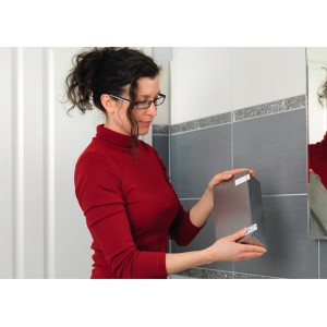 Žena pripevňuje strieborný predmet na stenu pomocou Tesa Powerstrips Large.