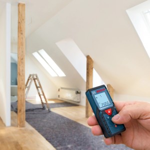 Laserový diaľkomer Bosch Professional GLM 40 v ruke pred staveniskom v podkroví.