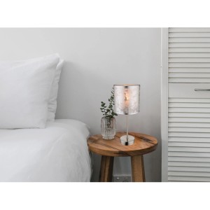 t.b.t. Nočná lampa so strieborným tienidlom na drevenom stolíku vedľa postele.