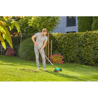 Muž vertikutuje trávnik s Gardena Combisystem vertikutátor-Boy 32 cm. Odstraňovanie machu v záhrade.