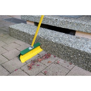 Žltá pazúrová metla (35 cm) so zelenou hlavou a žltou rukoväťou pri použití na dlažobných kockách.