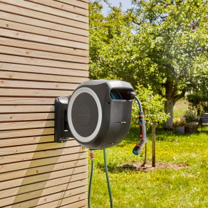 Nástenný box na hadicu Gardena XL s Comfort postrekovačom na drevenom dome. Záhradný hadicový vozík na zavlažovanie záhrady.