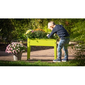 Jablkovo zelený kovový detský vyvýšený záhon Floraworld, osadený kvetmi, dieťa sa nad ním skláňa.