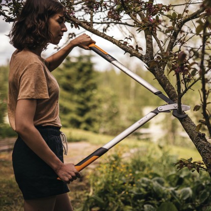Žena strihá konár s prevodovými nožnicami Fiskars LX99-L v záhrade.