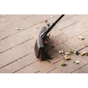 Všestranná metla Fiskars Solid M s PowerClean štetinami zametá lístie na dlažobných kockách.