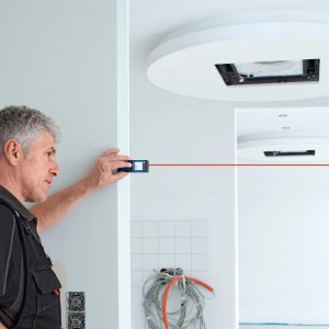 Remeselník meria miestnosť pomocou digitálneho laserového diaľkomeru Bosch Professional GLM 40.