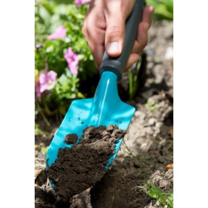 Kvetinová lopatka Gardena Classic v akcii: Ruka drží lopatku so zeminou v záhone.