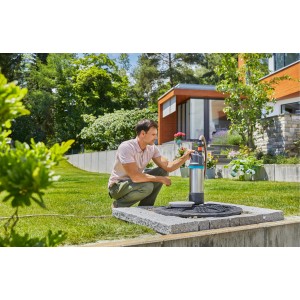 Muž obsluhuje strieborné záhradné čerpadlo na kamennom podstavci. Elektrické záhradné čerpadlo.