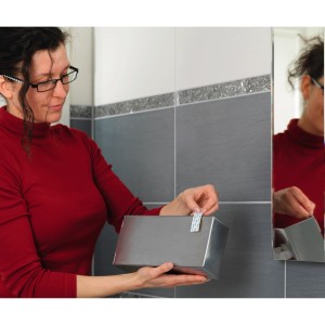 Žena pripevňuje striebornú nádobu na stenu pomocou Tesa Powerstrips.